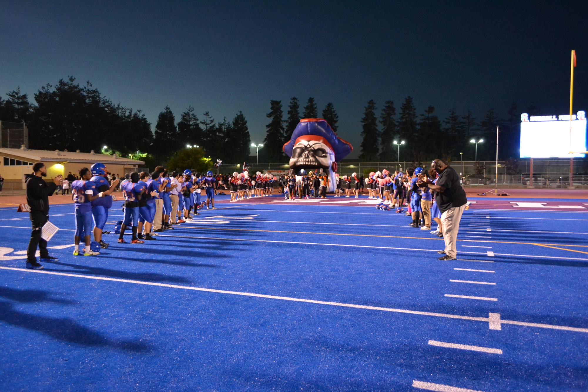 Football Coach Boom, the JV football team and cheerleaders welcome the seniors onto the field. 